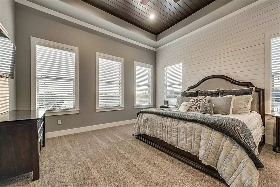 主卧室设有深色木质家具，地毯地板和覆盖木板的托盘天花板。