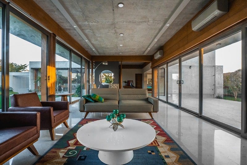 这是一间通风明亮的客厅，两侧各有一面玻璃墙，使灰色沙发和白色圆形咖啡桌更加明亮。