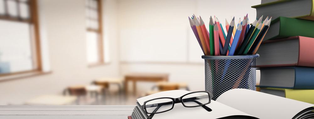 在一间空教室里，一堆书，一罐彩色铅笔，一副眼镜，上面是一本打开的书。