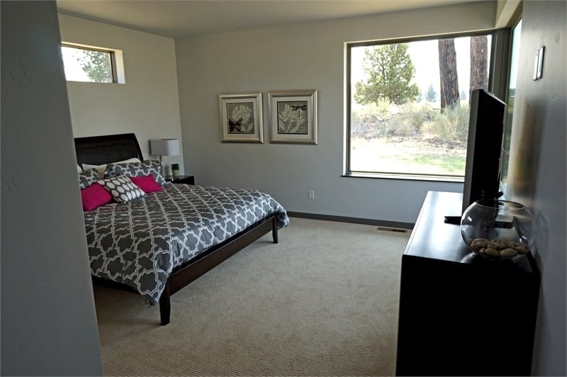 这间卧室有深色木家具，地毯地板，和俯瞰户外风景的落地窗。