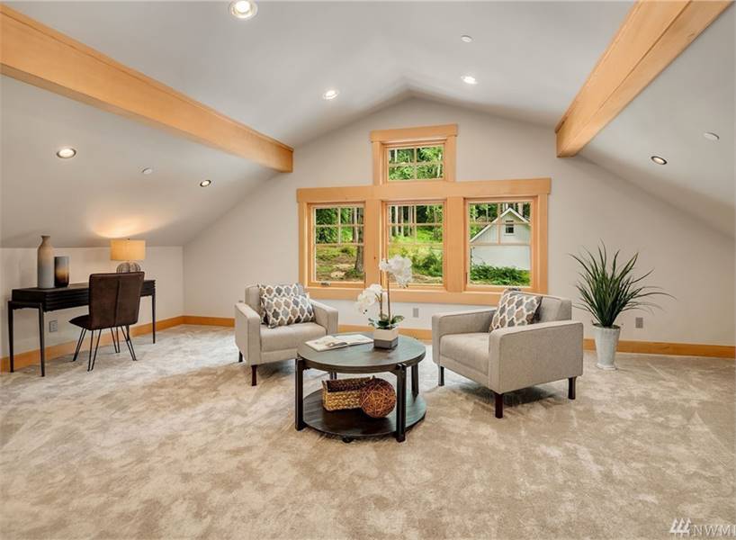 额外的房间里有米色的扶手椅，一个圆形的中心桌子，深色的木头桌子，地毯地板，和一个拱顶天花板，内衬乡村梁。