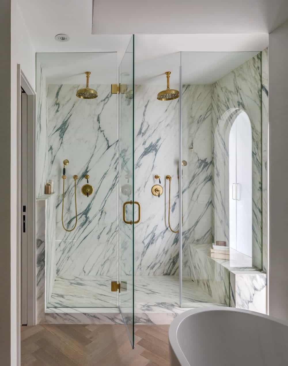 这是浴室的玻璃封闭淋浴区，白色大理石墙壁和地板使青铜固定装置脱颖而出。