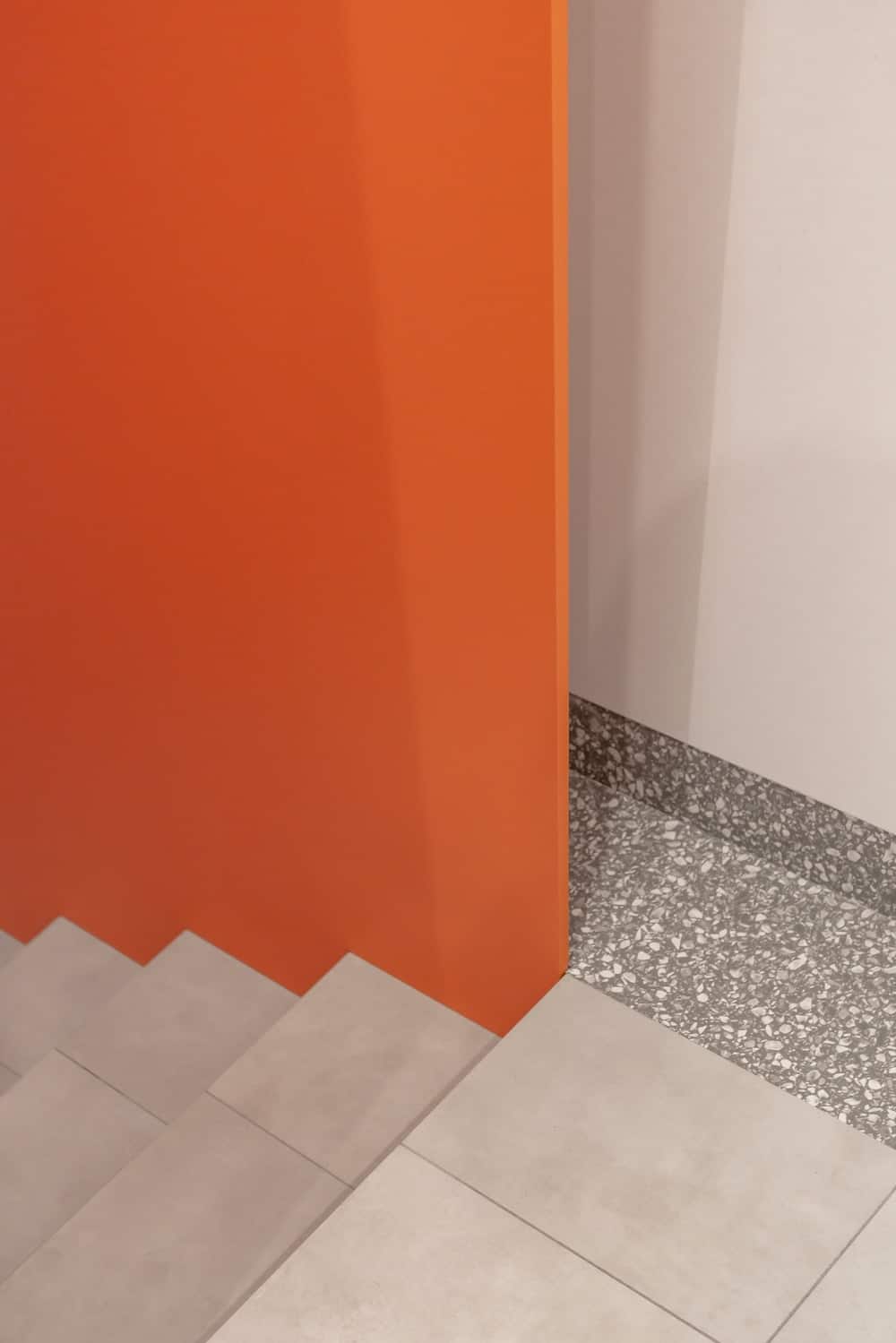 这是楼梯的另一个视角，浅灰色的台阶和地板与侧面亮橙色的墙壁形成对比。