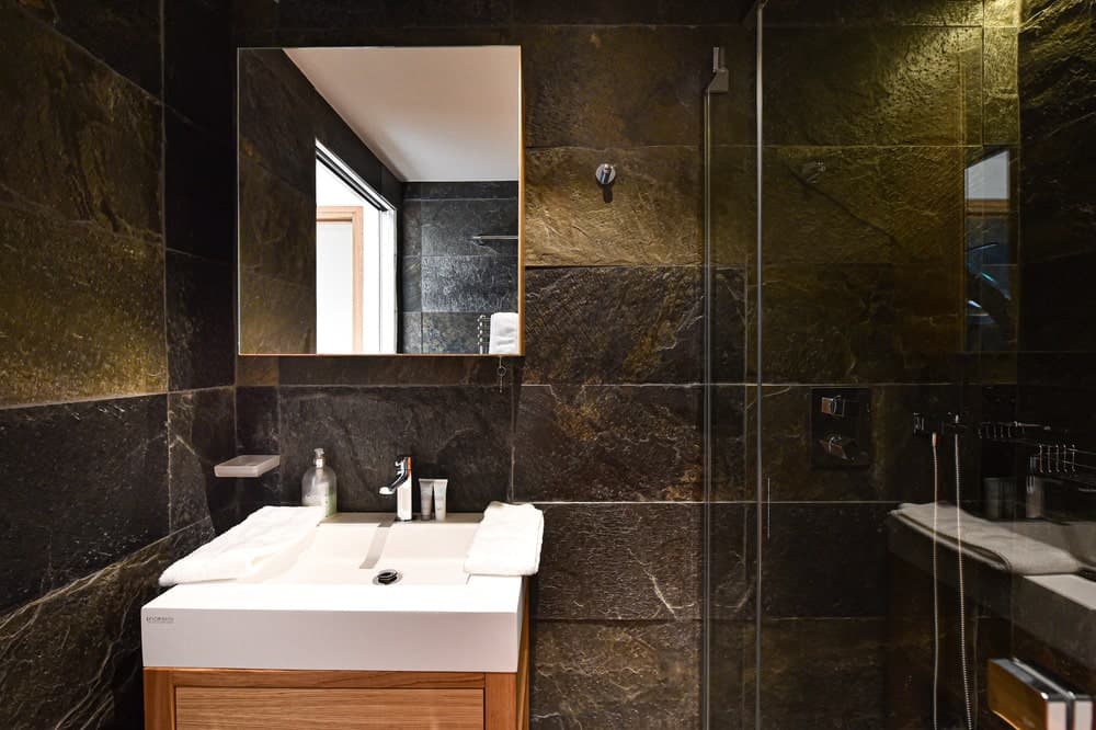 浴室里的小梳妆台与周围一致的深色大理石瓷砖形成鲜明对比。