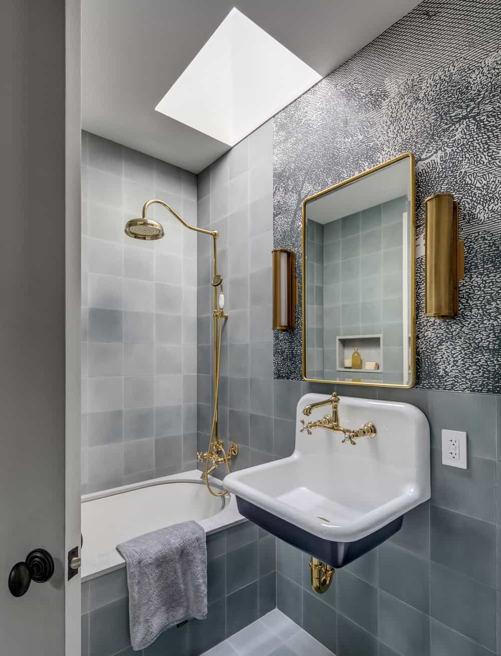 浴室墙壁上贴着一致的灰色瓷砖，使青铜固定装置和白瓷水槽和浴缸格外显眼。