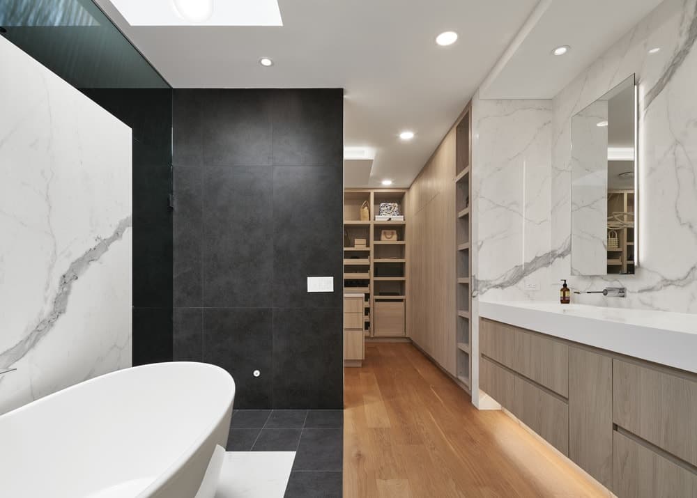这是一间浴室，有一个独立的大浴缸，靠在白色大理石墙上，与现代漂浮梳妆台的墙壁相匹配。