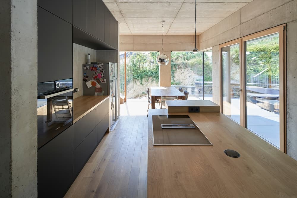 这是厨房区域的近距离观察，厨房岛台与硬木地板具有相同的木材色调，与对面的黑色橱柜搭配，嵌入到厚墙隔板中。