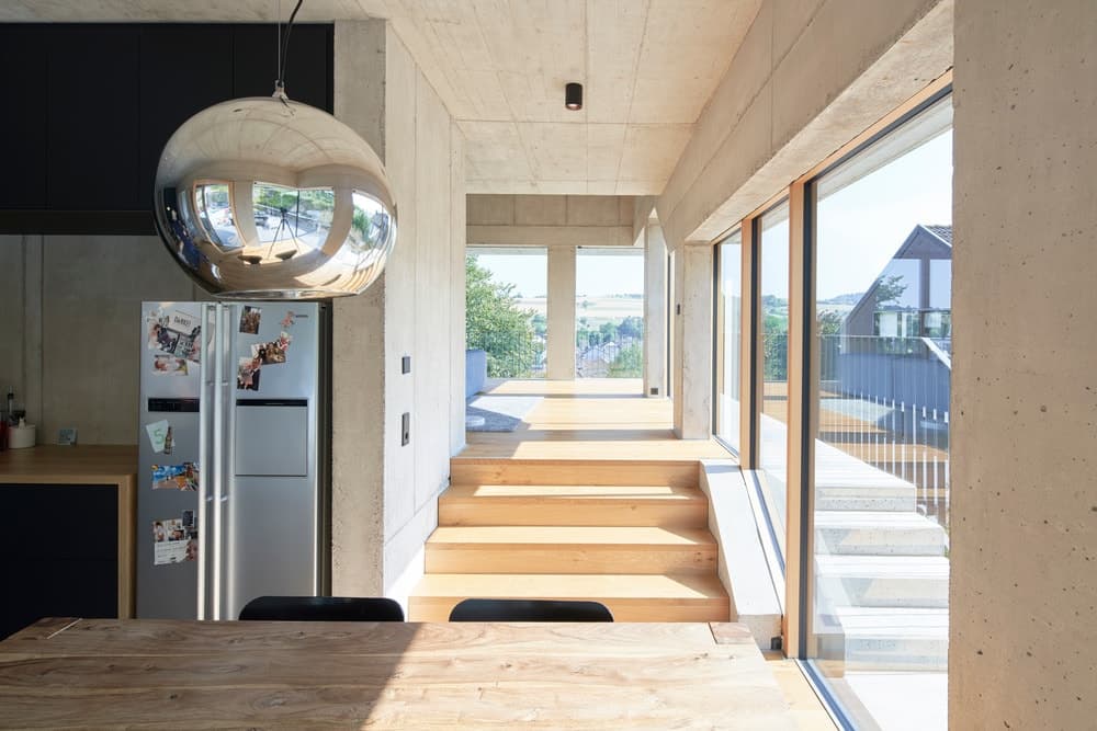 厨房边缘是用餐区，内有一张长方形餐桌，与硬木地板相呼应，硬木地板沐浴在玻璃墙的自然光中。