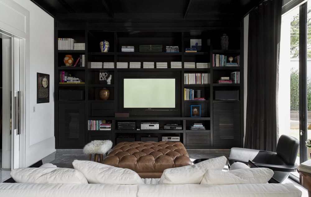 这是家庭娱乐室的近距离观察，在放置电视的米黄色组合沙发对面有一个巨大的黑色内置木结构。