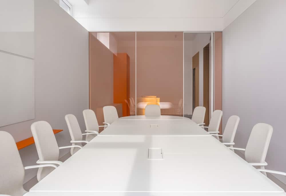 这是一张近距离观察的白色会议桌，光滑的表面被白色的办公椅包围着。