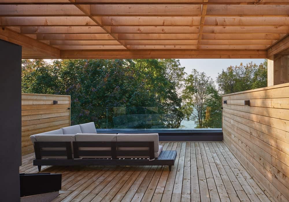 这是房子的木质甲板露台，有船板墙、地板和l型沙发上方的棚架。