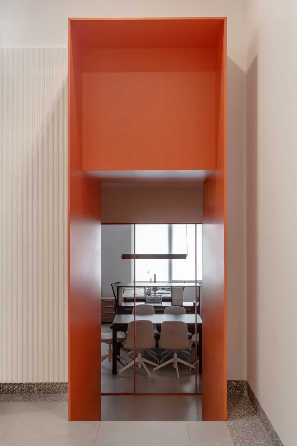 这是一个橙色的入口通道，通向更多的办公空间，远处有大型木制会议桌和办公桌。