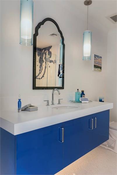 另一间浴室里有一个蓝色梳妆台，上面有一面拱形镜子和圆柱形吊坠。