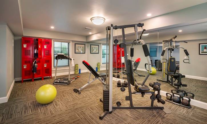 一个设备齐全的健身房，有红色储物柜，地毯地板和灰色墙壁。