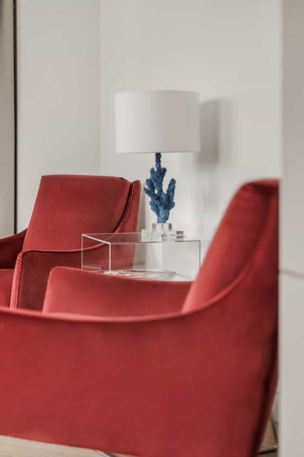 在这两张红色天鹅绒扶手椅之间是一张现代的玻璃边桌，上面有一盏台灯。