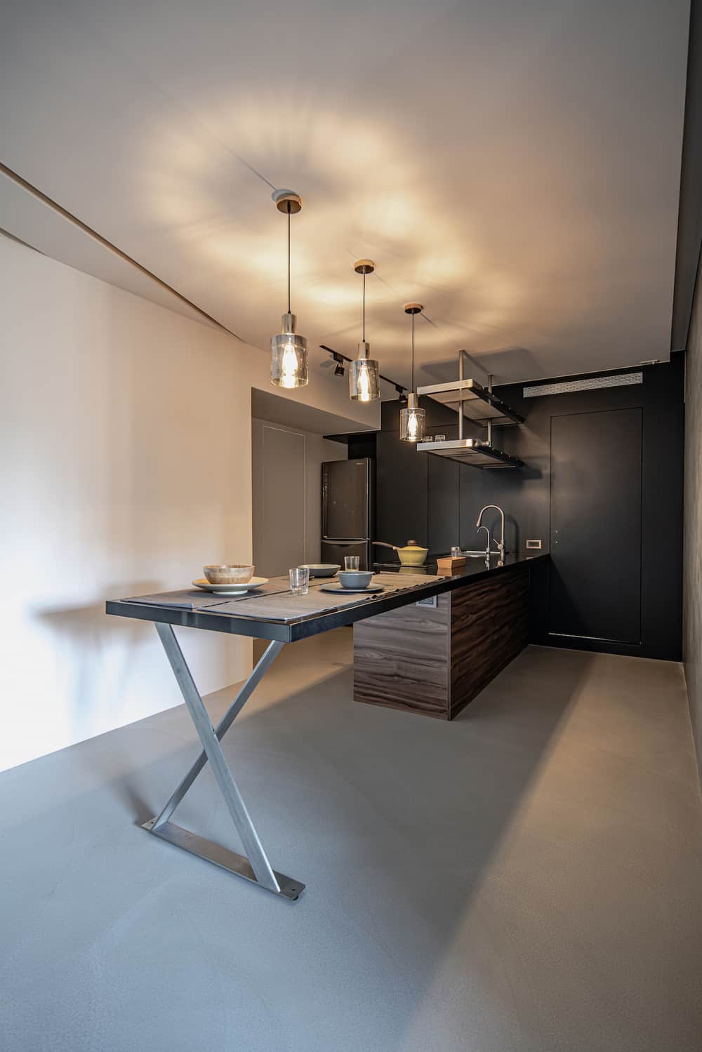 这是大厨房岛台的侧视图，远端有一套现代橱柜，黑色基调使不锈钢冰箱脱颖而出。
