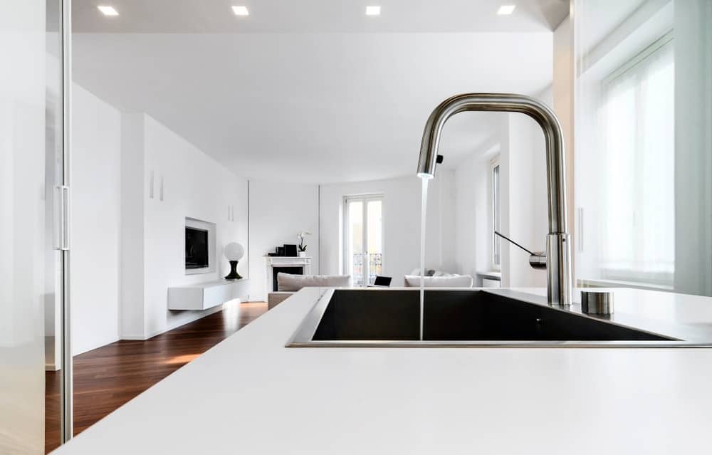 这是一个黑色的冲水式厨房水槽，在白色的台面上很显眼。