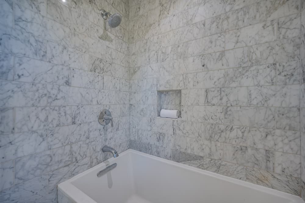 这是浴室的角落展示周围白色的浴缸,辅以白色大理石瓷砖墙上。图片由Toptenrealestatedeals.com。