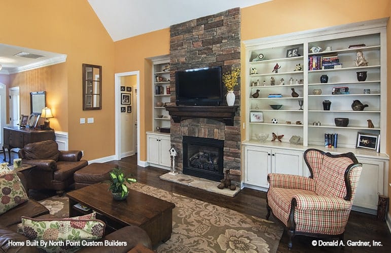 客厅里有皮革和格子座椅，一座石砌壁炉，平板电视和白色的嵌入式设备。
