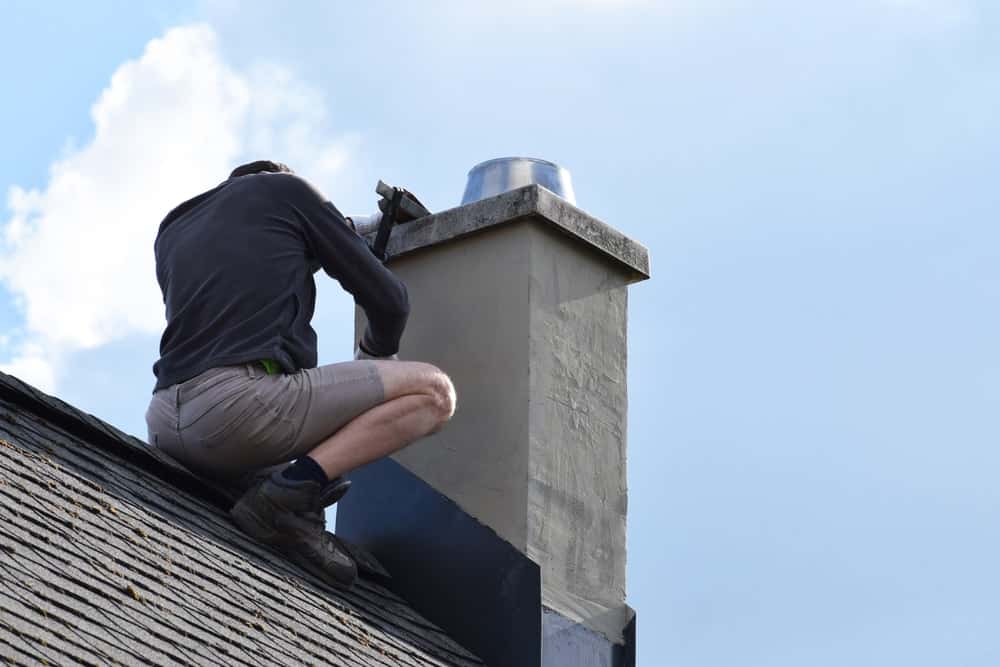 一个男人在屋顶上安装烟囱闪光装置。