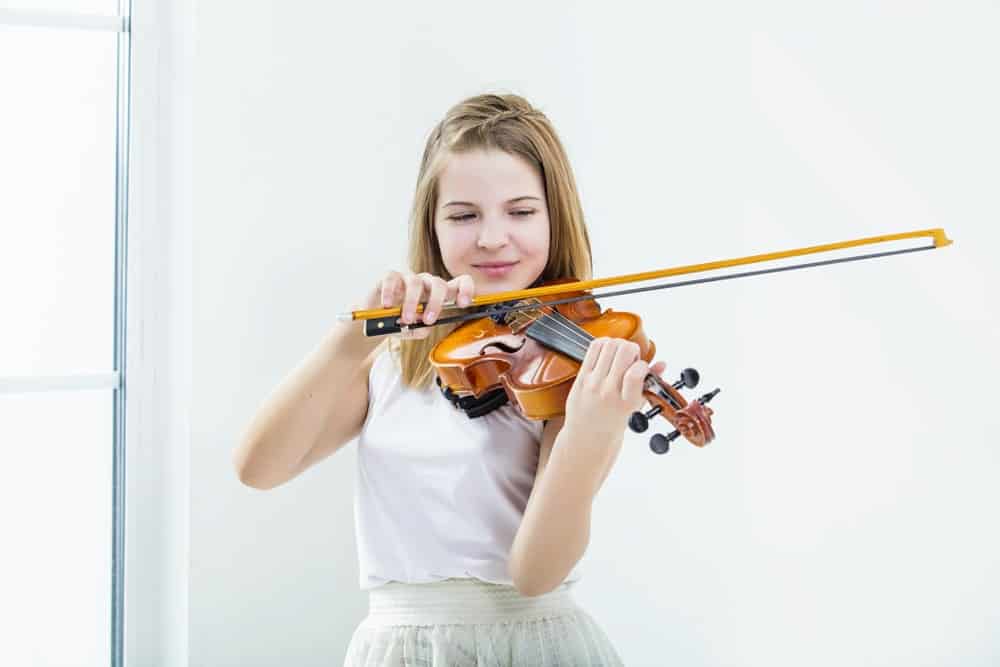 一个女孩在明亮的白色房间里拉小提琴。