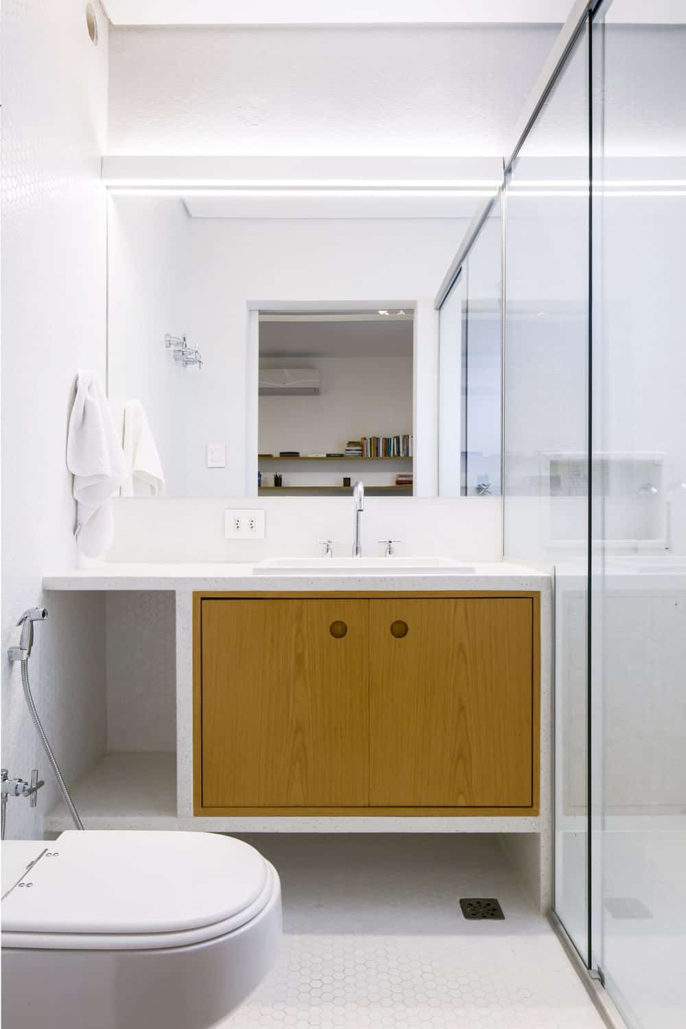 这间浴室有一个简单的现代梳妆台，在厕所和玻璃围成的淋浴区旁边有几个木橱柜。