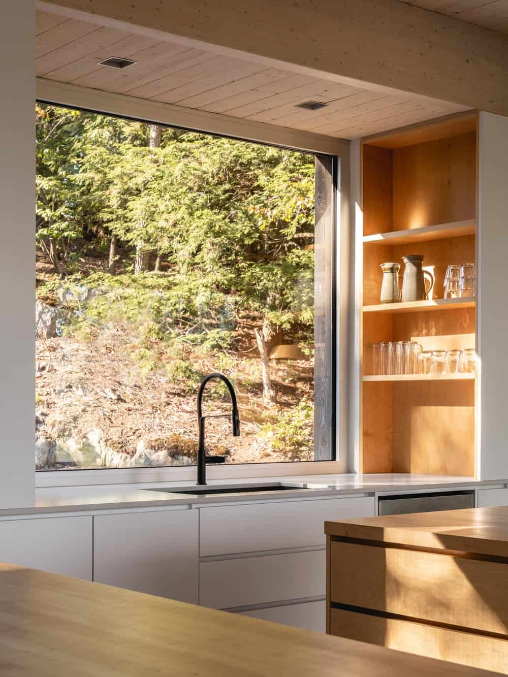 这是厨房的水龙头区域，白色的现代橱柜被大窗户照亮。