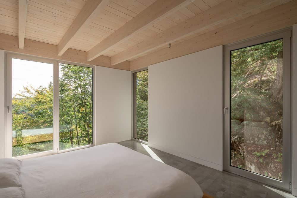 这是一间简单的卧室，在横梁天花板下有一张大床，木质色调，与玻璃墙外的绿色景观相辅相成。