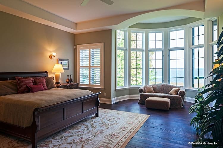 主卧室里有一张深色的木床，一张经典的区域地毯，一个有经典沙发和奥斯曼脚垫的休息区。