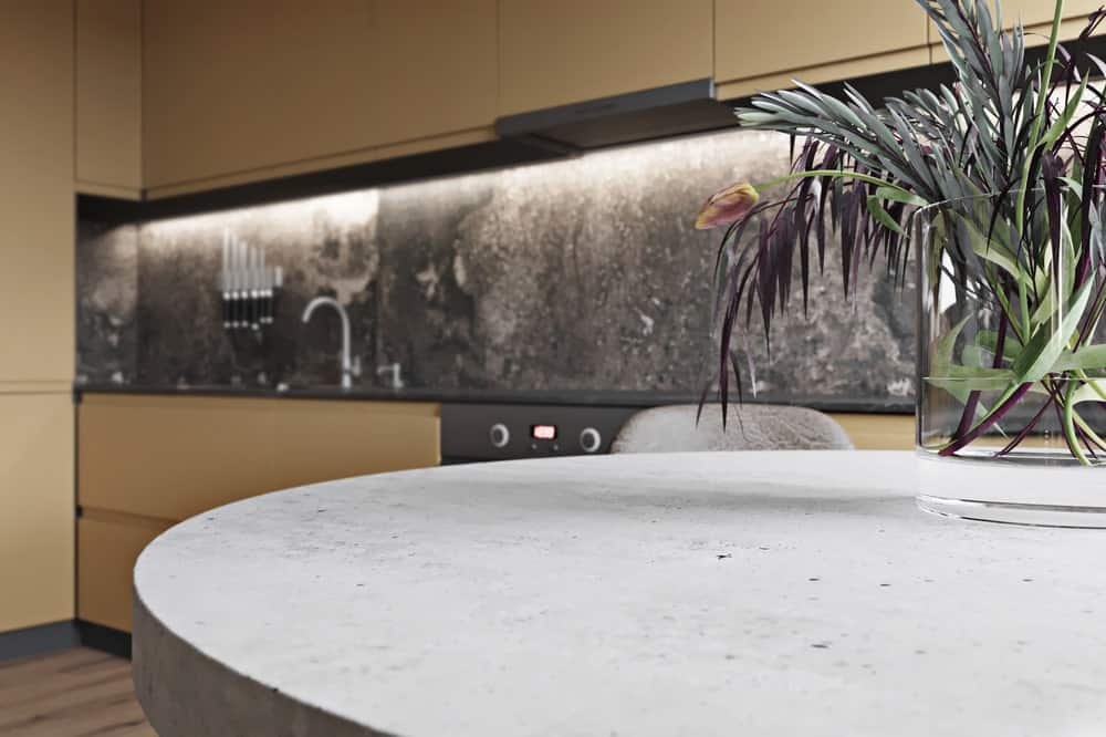 这是用餐区圆形餐桌的近距离观察，并可以看到一侧厨房的深色大理石台面和后挡板，上面有现代照明。