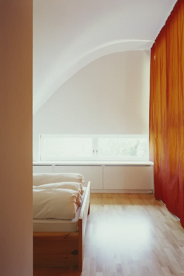卧室有浅色的硬木地板，白色的墙壁和被自然光线照亮的天花板使其更加明亮。