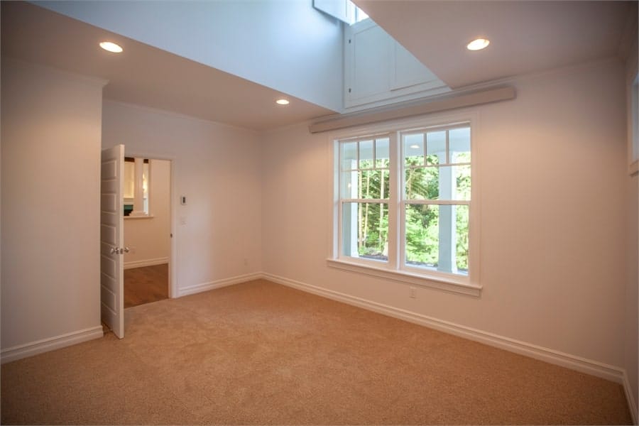 一扇白色的门通向一间卧室，卧室的墙壁是白色的，地板铺着米色的地毯。