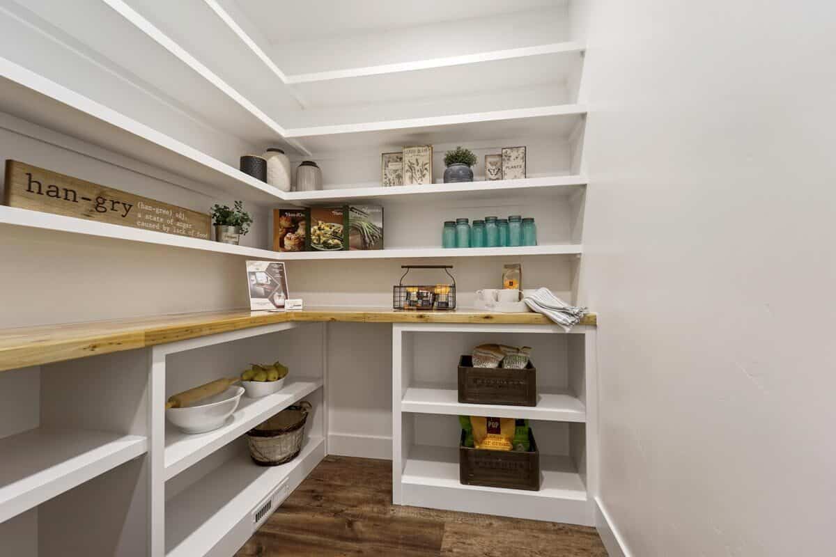 步入式食品储藏室里摆满了嵌壁式白色架子和木质台面。