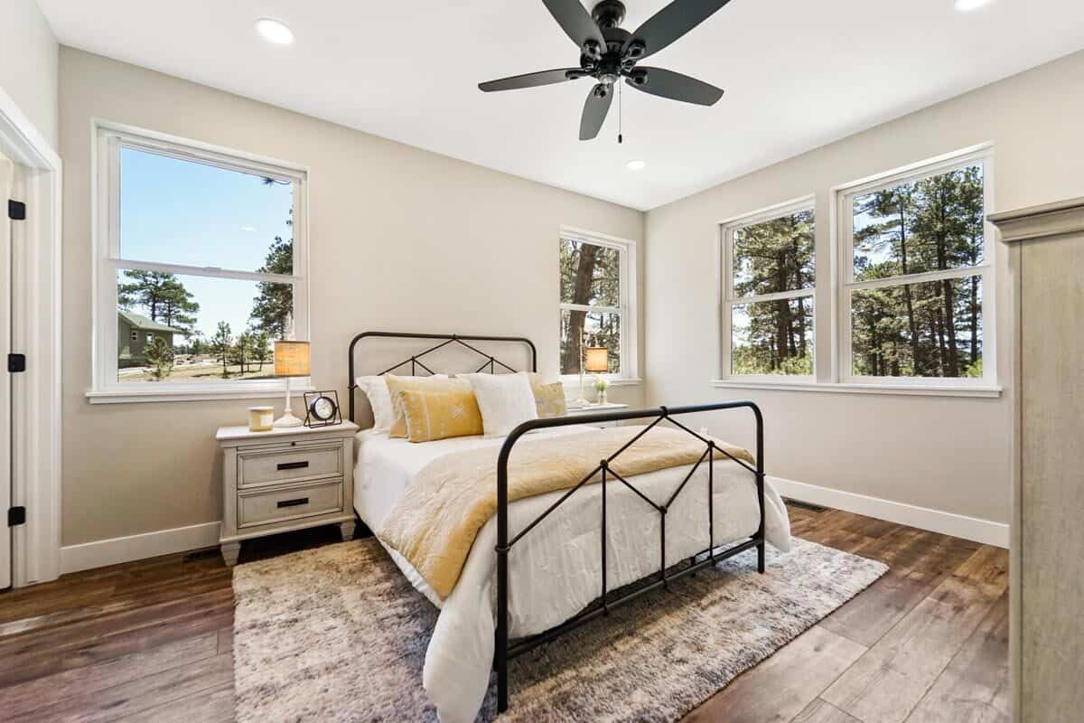 这间卧室提供一张金属床、白色床头柜和宽木板地板上的区域地毯。