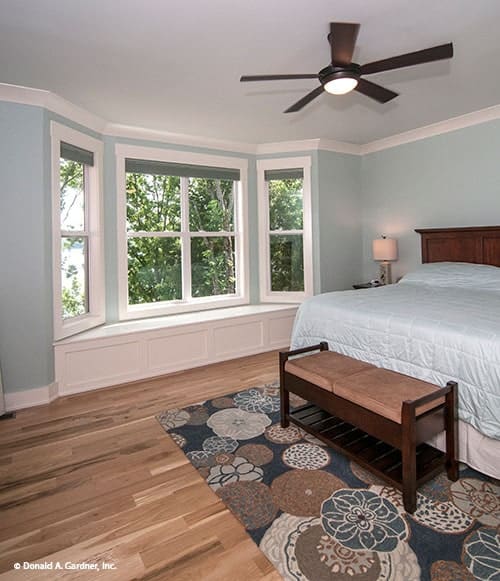 主卧室有木制家具、靠窗的座位和铺着花地毯的软垫长凳。