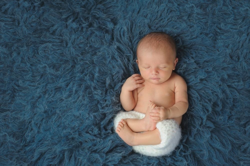 一个婴儿睡在蓝色粗毛地毯上。