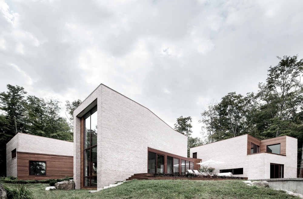 这是房子立面的侧视图，看起来像三个独立的结构，白色的外墙，木质的装饰和大的玻璃墙。