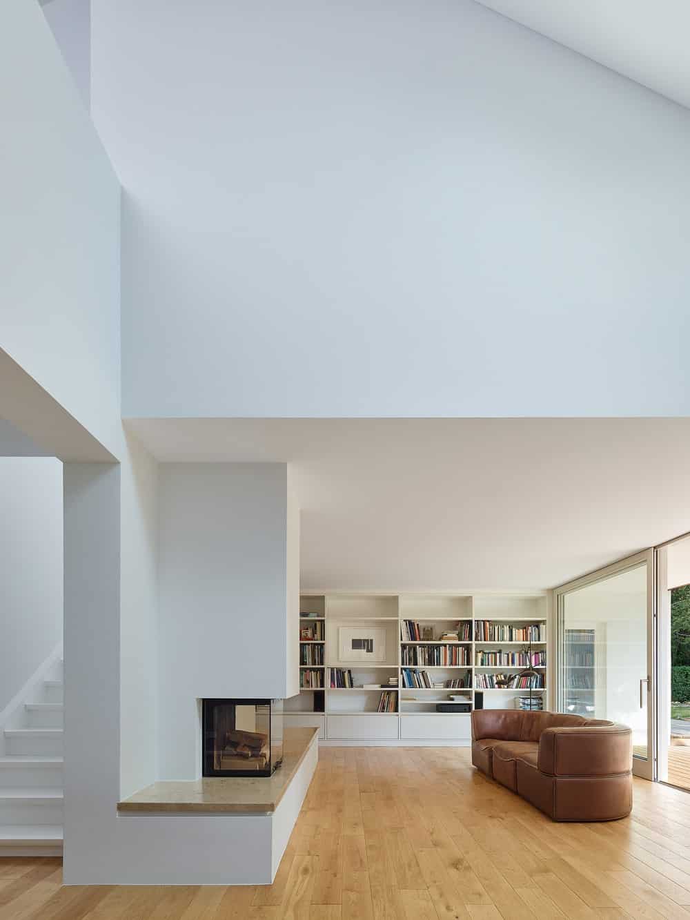 客厅明亮的白色墙壁、天花板和书架与组合沙发、壁炉和展示的书籍形成对比。