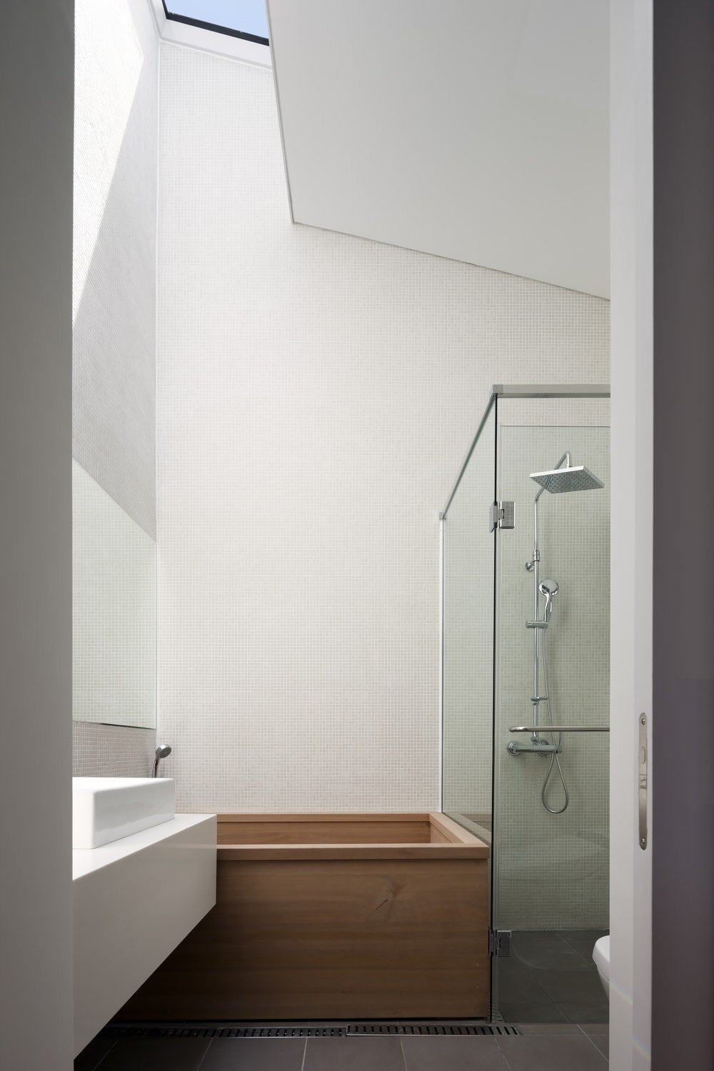 浴室里有一个玻璃封闭的淋浴区，白色水槽旁有一个木制浴缸。