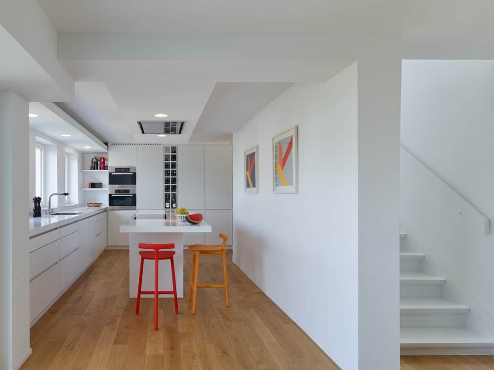 这是一个带有白色厨房岛台的厨房，让橙色的凳子显得格外显眼。这也给人一种现代和干净的氛围，与壁挂式艺术作品相匹配。