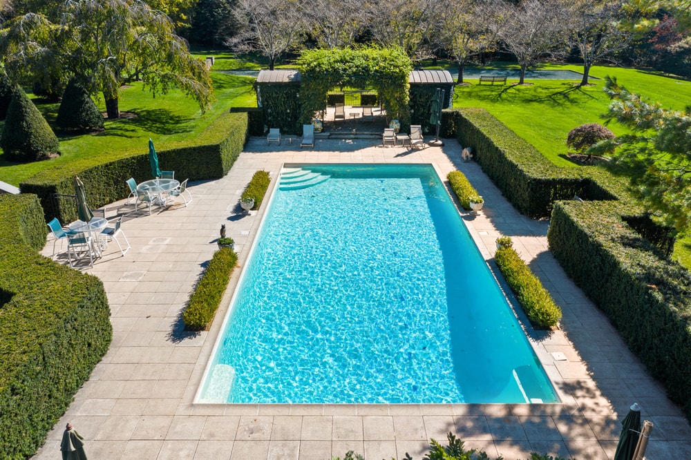 这是游泳池的鸟瞰图，周围是修剪整齐的灌木、树篱和砖砌的走道。图片来自Toptenrealestatedeals.com。