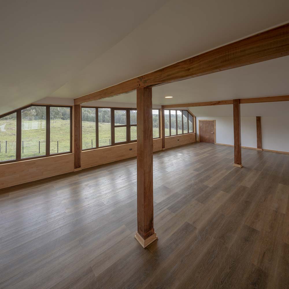 这是房子上层的另一个大房间，铺着宽阔的硬木地板，天花板上有与窗框相配的外露横梁。
