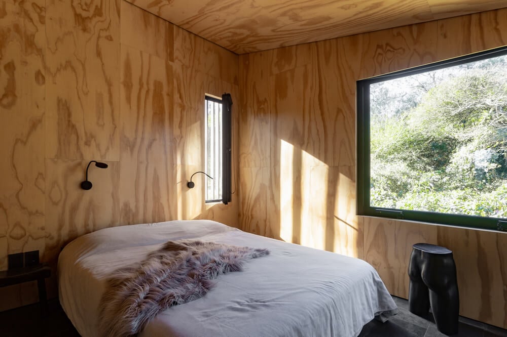 这是一间卧室，里面有一张平台床，上面有壁挂灯，在木墙和天花板的映衬下格外显眼。