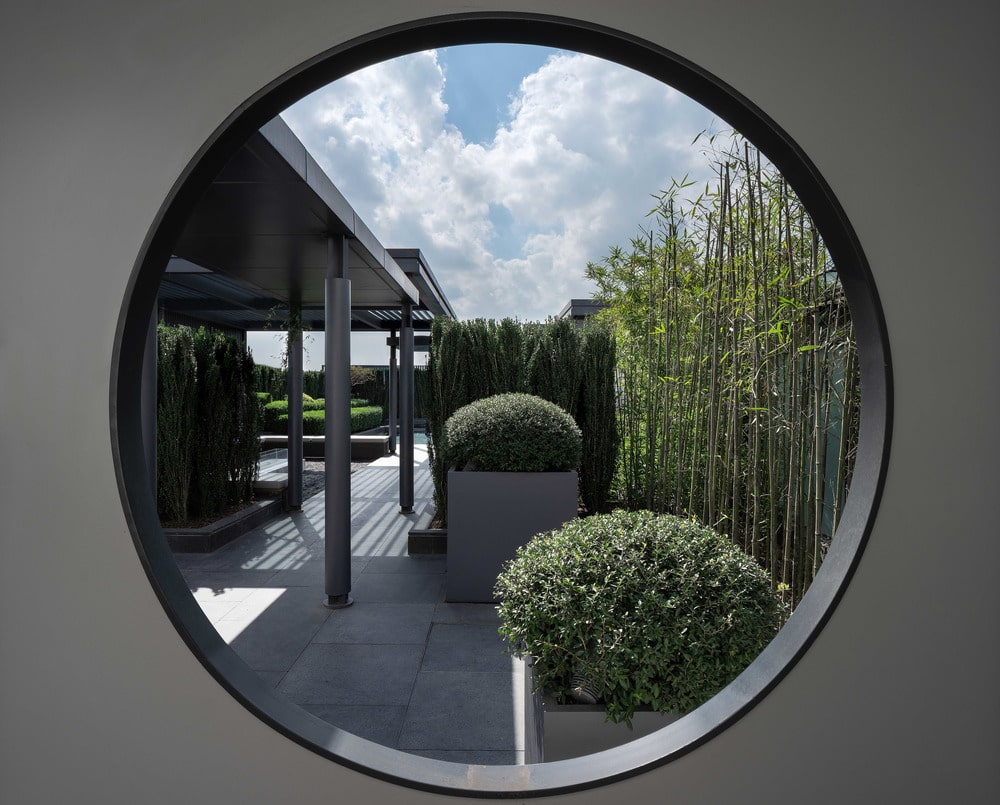 这是一个圆形的窗户，展示了外面的景观，以及盆栽和有盖的走道。