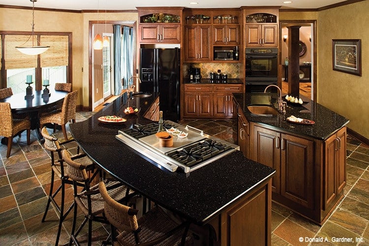用餐厨房与木制橱柜，黑色电器，花岗岩台面，和两个岛。