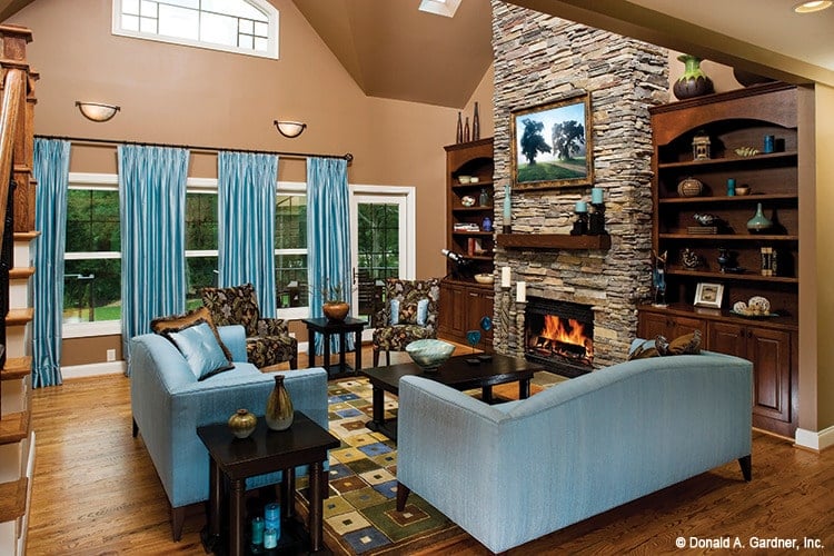 客厅里有石头壁炉，木制嵌壁式家具，有图案的椅子，蓝色沙发与窗帘相配。
