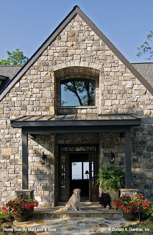 住宅入口有一个带顶棚的门廊和一个木质前门，周围有侧灯和横梁窗。