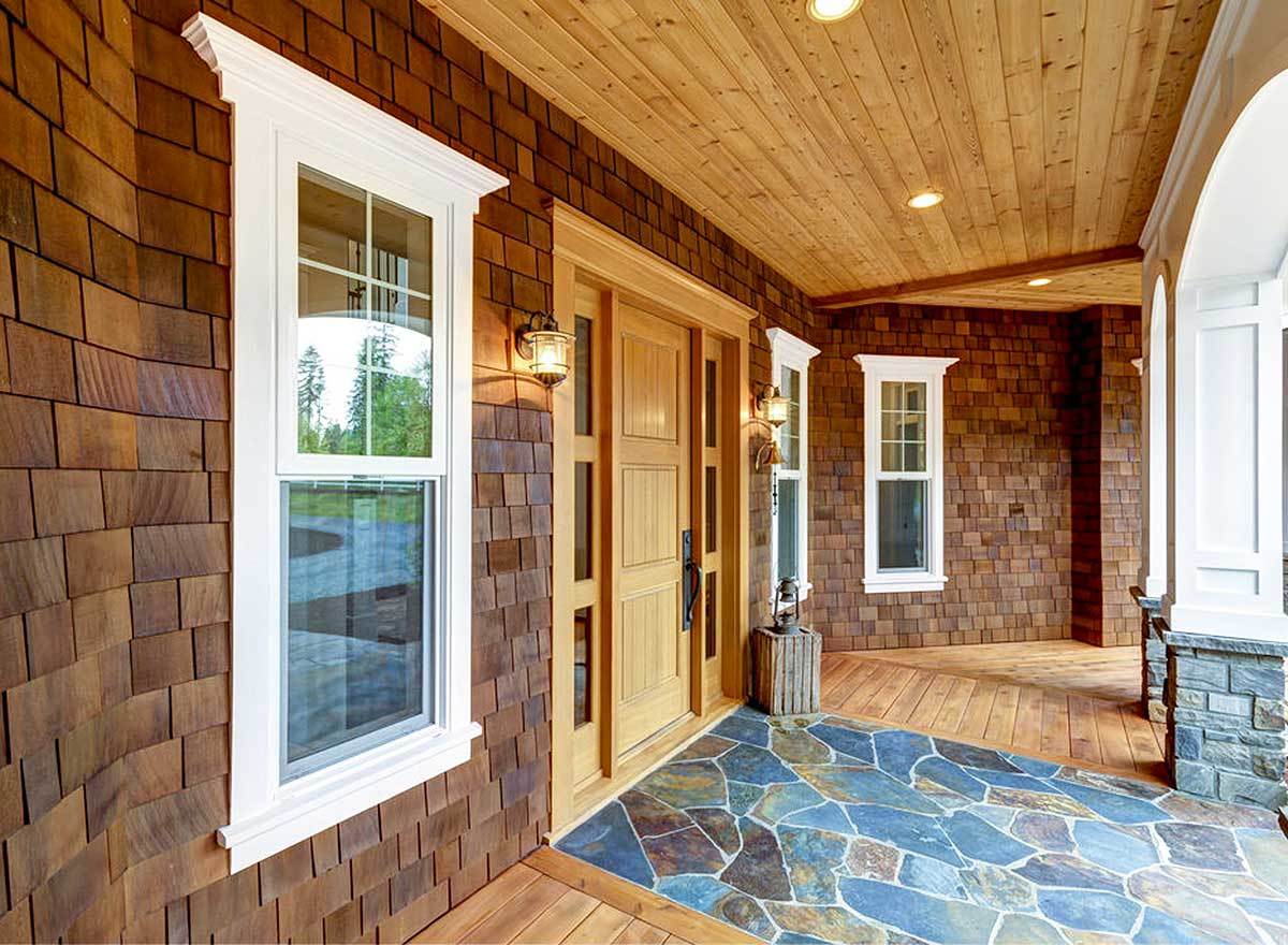 覆盖的门廊与木板天花板和木制入口门装饰侧灯。
