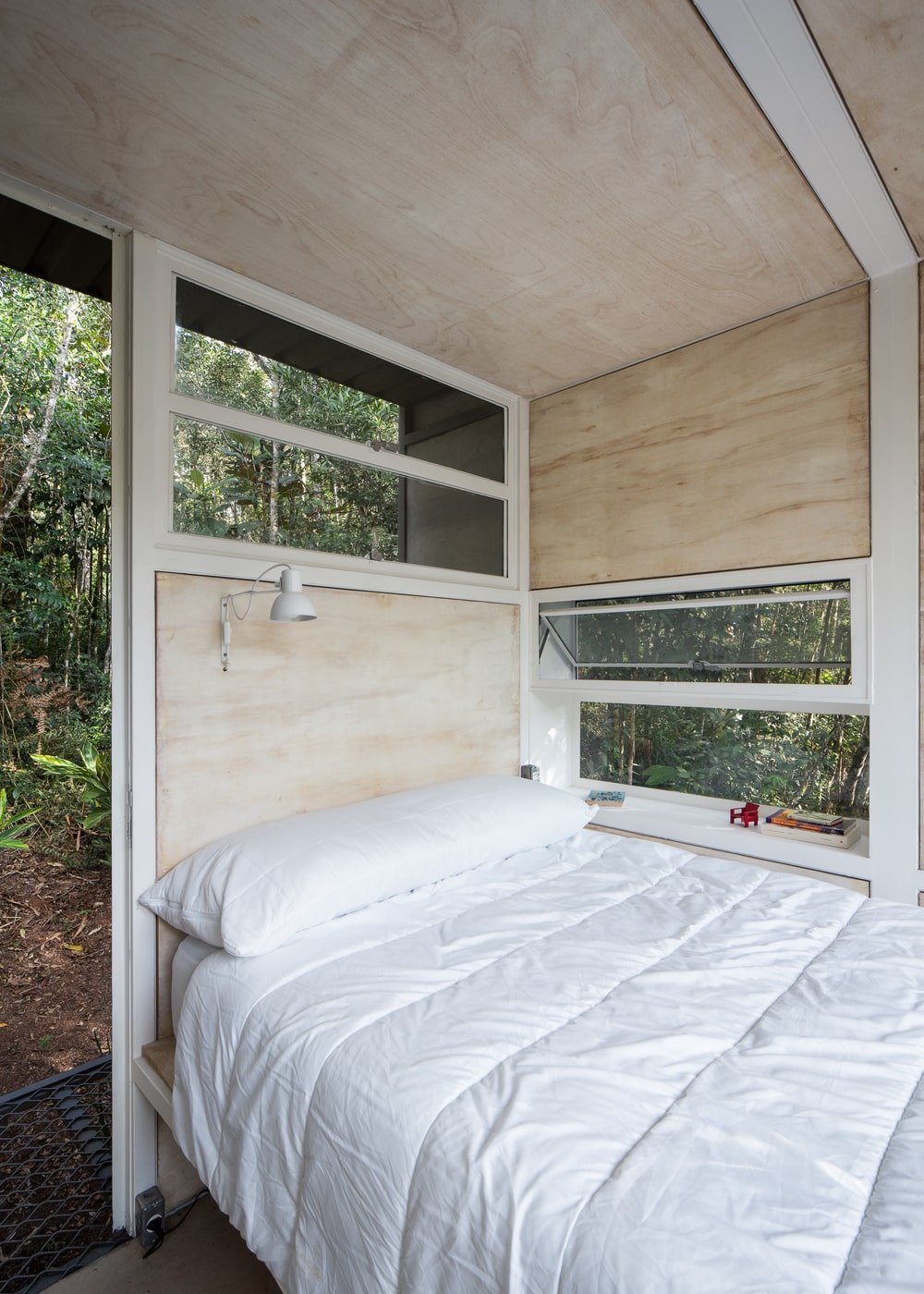 这是一间卧室，里面有一张白色的床，放在一个内置的木结构上，连接到墙上的窗户，可以看到外面的风景。