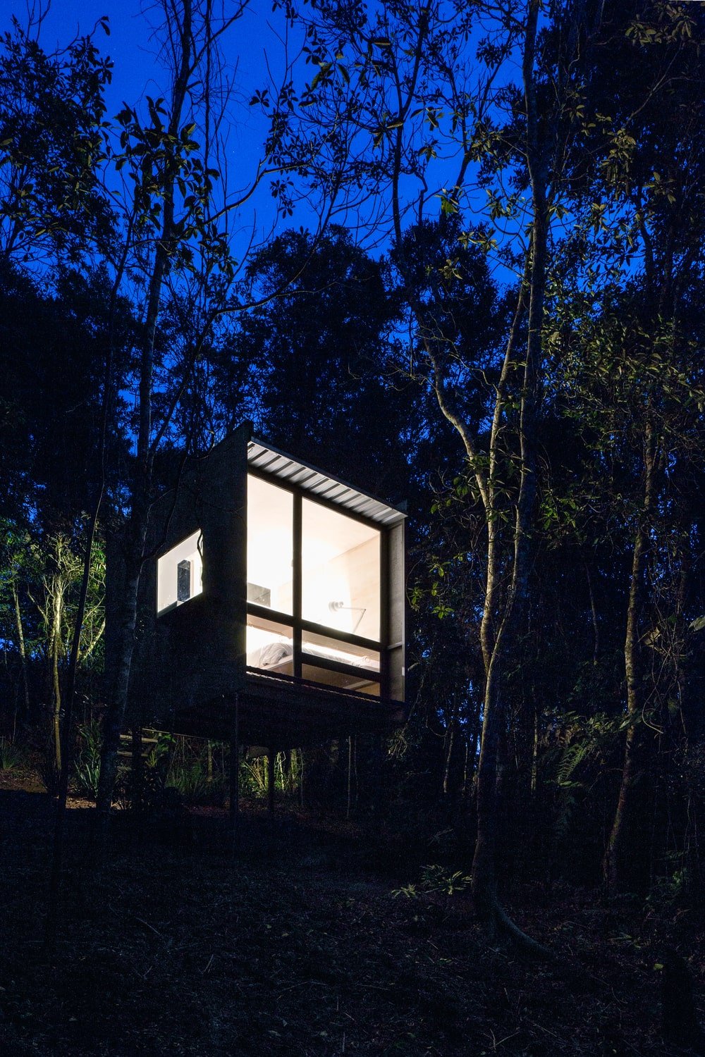这是房子的夜景，展示了玻璃墙壁的温暖光芒，使它在周围的景观中脱颖而出。